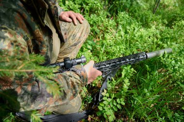 Tüfekli, kamuflaj kıyafetli avcı pusuda bekliyor. Ormanda pusuda bekleyen kamufle olmuş bir keskin nişancı. Askerler ormanda tüfekle saklanır..