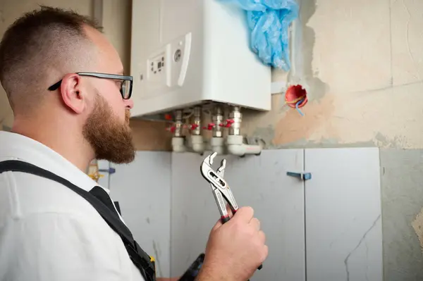 stock image Plumber Install a Boiler. Professional engineer installing gas boiler at home and checking the connections and pipes of the domestic heating system. Boiler Installation Service adjusting heating system.