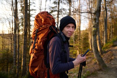 Tam teçhizatlı yürüyüşçü dağlarda güneşin erken doğuşunun tadını çıkarıyor. Bahar ormanında yürüyüş yapan sırt çantalı bir yürüyüşçü. Yürüyüş konsepti. Sırt çantalı bir gezgin ormanda yürüyor. Arkadan bak..
