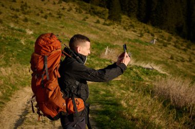Tam donanımlı bir yürüyüşçü sabahın erken saatlerinde dağlarda akıllı telefondan gündoğumunun fotoğraflarını çekiyor. Cep telefonlu bir adam dağ yolunda güneşin doğuşunun tadını çıkarıyor. Görüntüyü kapat
