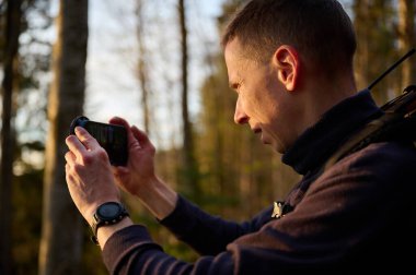 Tam donanımlı bir yürüyüşçü sabahın erken saatlerinde dağlarda akıllı telefondan gündoğumunun fotoğraflarını çekiyor. Cep telefonlu bir adam dağ yolunda güneşin doğuşunun tadını çıkarıyor. Görüntüyü kapat