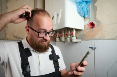 Tesisatçı Boiler.Profesyonel mühendis eve gaz kazanı kuruyor ve akıllı telefon kullanarak iç ısıtma sisteminin bağlantılarını ve borularını kontrol ediyor. Kazan Kurma Servisi ayarlaması.