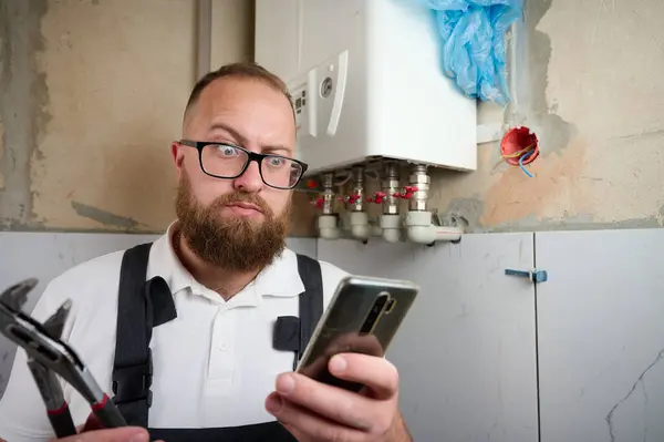 stock image Plumber Install Boiler.Professional engineer installing gas boiler at home and checking the connections and pipes of the domestic heating system using smartphone.Boiler Installation Service adjusting.