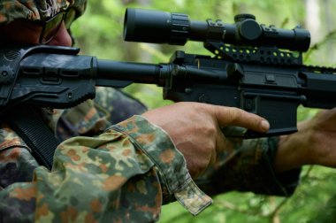 Tüfekli, kamuflaj kıyafetli avcı pusuda bekliyor. Ormanda pusuda bekleyen kamufle olmuş bir keskin nişancı. Askerler ormanda tüfekle saklanır..