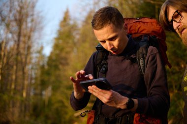 Tam donanımlı bir yürüyüşçü sabahın erken saatlerinde dağlarda akıllı telefondan gündoğumunun fotoğraflarını çekiyor. Cep telefonlu bir adam dağ yolunda güneşin doğuşunun tadını çıkarıyor. Görüntüyü kapat