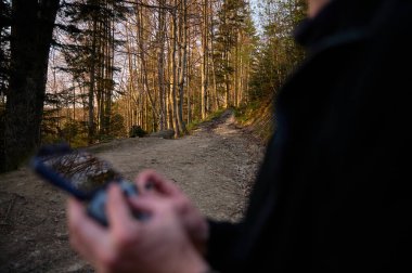İHA operatörünün elinde uzaktan kumandayla mavi görüşünü kapatın. Gezgin, uzaktan kumandayla dağların üzerinden uçan bir dronu kontrol ediyor. Hava görüntüleri ve fotoğrafçılık çekimleri. Gün doğumu