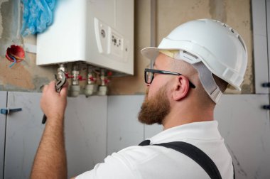 Tesisatçı bir kazan kurdu. Profesyonel mühendis eve gaz kazanı kuruyor ve iç ısıtma sisteminin bağlantılarını ve borularını kontrol ediyor. Isıtma sistemini ayarlayan Kazan Kurma Servisi.