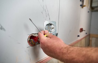Profesyonel elektrikçi yeni bir evde tornavida kullanarak duvara elektrik prizi takıyor. Evde elektrik tamiratı var. Elektrikçi prizi elektrikli tornavidayla bağlıyor.