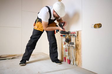 Man adjusting the heating system in a new apartment. Plumber adjusting heat on the central system valves. Service man adjusting house heating system. Underfloor heating system. Man checking pipe clipart