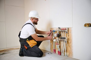 Man adjusting the heating system in a new apartment. Plumber adjusting heat on the central system valves. Service man adjusting house heating system. Underfloor heating system. Man checking pipe clipart