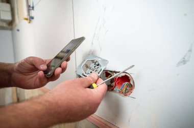 Profesyonel elektrikçi yeni bir evde tornavida kullanarak duvara elektrik prizi takıyor. Evde elektrik tamiratı var. Elektrikçi prizi elektrikli tornavidayla bağlıyor.