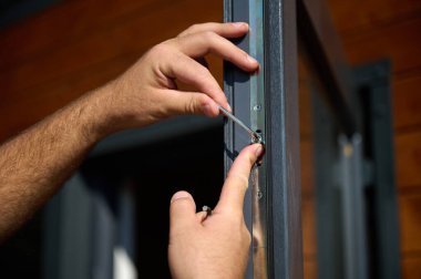 Yeni bir inşaat sahasına kapı ve pencere döşeyen işçilerin yakın görüntüsü. Büyülü anahtarı olan üniformalı bir adam yeni güzel evin ön cam kapısını ve pencerelerini ayarlıyor. Ekin görünümü.