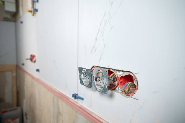 Profesyonel elektrikçi yeni bir evde tornavida kullanarak duvara elektrik prizi takıyor. Evde elektrik tamiratı var. Elektrikçi prizi elektrikli tornavidayla bağlıyor.