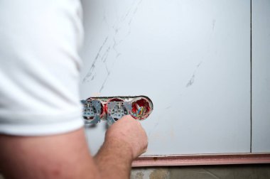 Profesyonel elektrikçi yeni bir evde tornavida kullanarak duvara elektrik prizi takıyor. Evde elektrik tamiratı var. Elektrikçi prizi elektrikli tornavidayla bağlıyor.