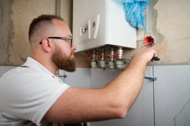 Tesisatçı bir kazan kurdu. Profesyonel mühendis eve gaz kazanı kuruyor ve iç ısıtma sisteminin bağlantılarını ve borularını kontrol ediyor. Isıtma sistemini ayarlayan Kazan Kurma Servisi.