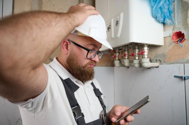 Tesisatçı Boiler.Profesyonel mühendis eve gaz kazanı kuruyor ve akıllı telefon kullanarak iç ısıtma sisteminin bağlantılarını ve borularını kontrol ediyor. Kazan Kurma Servisi ayarlaması.