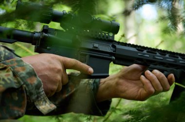 Tüfekli, kamuflaj kıyafetli avcı pusuda bekliyor. Ormanda pusuda bekleyen kamufle olmuş bir keskin nişancı. Askerler ormanda tüfekle saklanır..