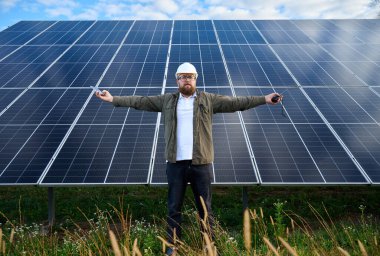 Üniformalı bir mühendis, güneş istasyonunun yakınında elinde telsizle el hareketi yapıyor. Güneş çiftliğinde el kol hareketleri yapan bir adam. Güneş ve yenilenebilir enerji kavramı.