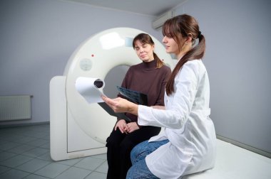 Radyolog kadın hastaya röntgen raporu gösteriyor. Tomografi odasında kendine güvenen güzel bir doktora danışmanlık yapıyor. MRI uzmanı durumu açıklıyor. Doktor ve hasta klinikte..