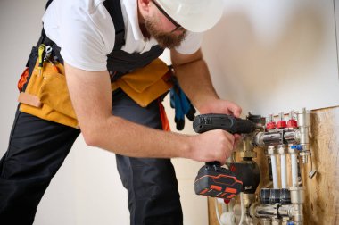Adam yeni bir dairede ısıtma sistemini ayarlıyor. Tesisatçı merkezi sistem vanalarındaki ısıyı ayarlıyor. Servis elemanı ısıtma sistemini ayarlıyor. Yeraltı ısıtma sistemi. Adam boruyu kontrol ediyor