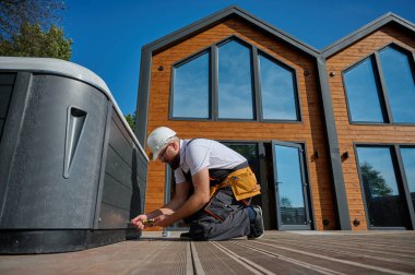 Tesisatçı jakuzi kuruyor. Kaplıca teknisyeni jakuzi yapıyor. Küvet tesisatı. Tesisatçı kaplıcayı tamir ediyor. Üniformalı bir uzman, şık bir bahçe avlusunda bir jakuzi hazırlıyor ve inceliyor..