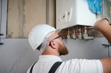 Tesisatçı bir kazan kurdu. Profesyonel mühendis eve gaz kazanı kuruyor ve iç ısıtma sisteminin bağlantılarını ve borularını kontrol ediyor. Isıtma sistemini ayarlayan Kazan Kurma Servisi.