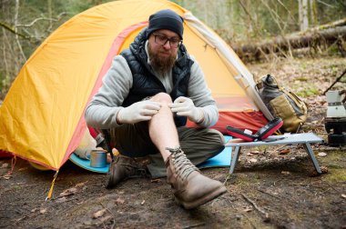Ormandaki çadırın yakınındaki ilk yardım çantasını kullanan yaralı bacaklı bir yürüyüşçü. Stresli bir yürüyüşçü dağda kırık diziyle tek başına şikayet ediyor..