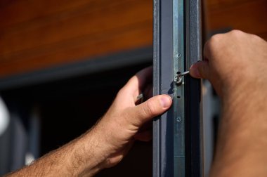 Yeni bir inşaat sahasına kapı ve pencere döşeyen işçilerin yakın görüntüsü. Büyülü anahtarı olan üniformalı bir adam yeni güzel evin ön cam kapısını ve pencerelerini ayarlıyor. Ekin görünümü.