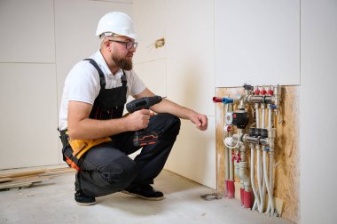 Adam yeni bir dairede ısıtma sistemini ayarlıyor. Tesisatçı merkezi sistem vanalarındaki ısıyı ayarlıyor. Servis elemanı ısıtma sistemini ayarlıyor. Yeraltı ısıtma sistemi. Adam boruyu kontrol ediyor