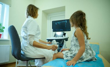 Pediatrik ultrason taraması. Çocuk ultrasonu. Çocuk doktoru dizini tarıyor. Doktorun çocuk için bacak sonogramı çekerken yan görüntüsü. İskelet sisteminin ultrason incelemesi. Eklem hastalıkları konsepti
