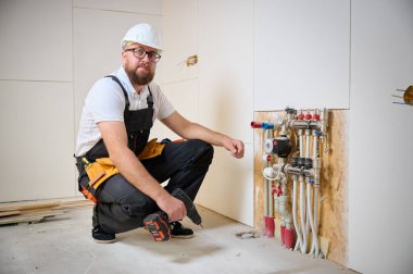 Adam yeni bir dairede ısıtma sistemini ayarlıyor. Tesisatçı merkezi sistem vanalarındaki ısıyı ayarlıyor. Servis elemanı ısıtma sistemini ayarlıyor. Yeraltı ısıtma sistemi. Adam boruyu kontrol ediyor