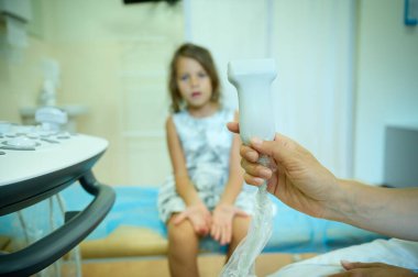 Çocuk doktoru ortopedist ultrason sondasıyla genç bir kıza danışıp muayene ediyor. Modern, zararsız muayene. Gençlerin sağlığı. Erken teşhis. Çocukluk korkuları. Klinik kavramı.
