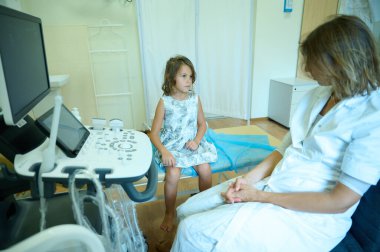Çocuk doktoru ortopedist ultrason sondasıyla genç bir kıza danışıp muayene ediyor. Modern, zararsız muayene. Gençlerin sağlığı. Erken teşhis. Çocukluk korkuları. Klinik kavramı.