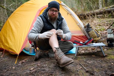 Ormandaki çadırın yakınındaki ilk yardım çantasını kullanan yaralı bacaklı bir yürüyüşçü. Stresli bir yürüyüşçü dağda kırık diziyle tek başına şikayet ediyor..