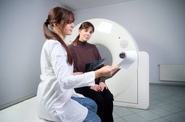 Radyolog kadın hastaya röntgen raporu gösteriyor. Tomografi odasında kendine güvenen güzel bir doktora danışmanlık yapıyor. MRI uzmanı durumu açıklıyor. Doktor ve hasta klinikte..