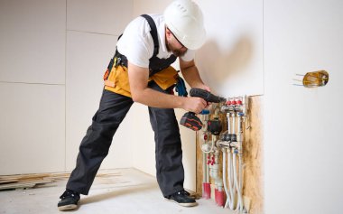Adam yeni bir dairede ısıtma sistemini ayarlıyor. Tesisatçı merkezi sistem vanalarındaki ısıyı ayarlıyor. Servis elemanı ısıtma sistemini ayarlıyor. Yeraltı ısıtma sistemi. Adam boruyu kontrol ediyor