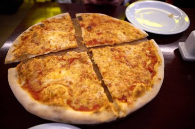 Masadaki pizzanın görüntüsünü kapat. Lezzetli yemek. İnsanlar pizzacıda bir araya gelip lezzetli İtalyan yemeklerini paylaşırken eğleniyorlar.