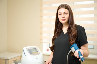 Klinikte tıbbi kıyafet giymiş genç bir kız rehabilitasyon uzmanı elinde şok dalgası terapisi için bir cihaz tutuyor. Yaralardan sonra iyileşme kavramı. Extracorporeal Shockwave Terapisi