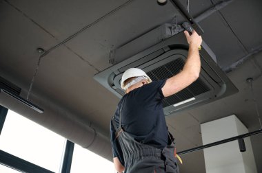 Sakallı adam merdivende duruyor ofise klima yerleştiriyor. Modern binada tavana monte edilmiş klima. Çatı katı tarzı. Endüstriyel iç tasarım. Teknisyen servisi.