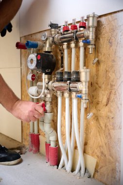 Adam yeni bir dairede ısıtma sistemini ayarlıyor. Tesisatçı merkezi sistem vanalarındaki ısıyı ayarlıyor. Servis elemanı ısıtma sistemini ayarlıyor. Yeraltı ısıtma sistemi. Ekin görünümü