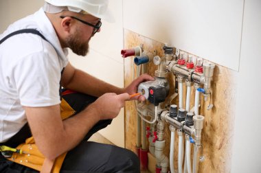 Adam yeni bir dairede ısıtma sistemini ayarlıyor. Tesisatçı merkezi sistem vanalarındaki ısıyı ayarlıyor. Servis elemanı ısıtma sistemini ayarlıyor. Yeraltı ısıtma sistemi. Ekin görünümü