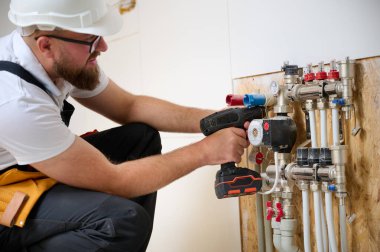 Adam yeni bir dairede ısıtma sistemini ayarlıyor. Tesisatçı merkezi sistem vanalarındaki ısıyı ayarlıyor. Servis elemanı ısıtma sistemini ayarlıyor. Yeraltı ısıtma sistemi. Adam boruyu kontrol ediyor
