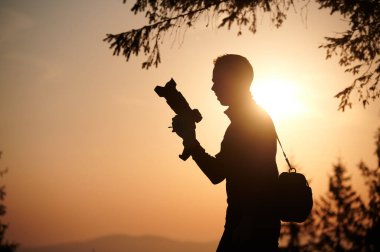 Şafakta fotoğraf çeken bir fotoğrafçının silueti. Güneş doğarken, dağ tepesinde elinde kamera olan bir turist. İnsan, güneşin batışında dağların fotoğrafını çeker..