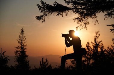 Şafakta fotoğraf çeken bir fotoğrafçının silueti. Güneş doğarken, dağ tepesinde elinde kamera olan bir turist. İnsan, güneşin batışında dağların fotoğrafını çeker..