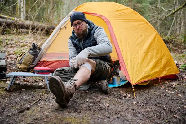 Ormandaki çadırın yakınındaki ilk yardım çantasını kullanan yaralı bacaklı bir yürüyüşçü. Stresli bir yürüyüşçü dağda kırık diziyle tek başına şikayet ediyor. Gezgin yaralanmadan sonra bacağını bandajlıyor.