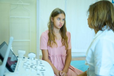 Çocuk doktoru ortopedist ultrason sondasıyla genç bir kıza danışıp muayene ediyor. Modern, zararsız muayene. Gençlerin sağlığı. Erken teşhis. Çocukluk korkuları. Klinik kavramı.