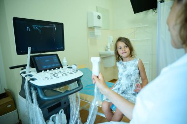 İlgili çocuk doktoru elinde ultrason sondasıyla küçük bir çocuğa klinikte danışmanlık yapıyor. Doktor ultrason tarayıcısını ultrason işlemi için hazırlıyor. Tıp bürosu. Ultrason taraması için hazırlanılıyor.