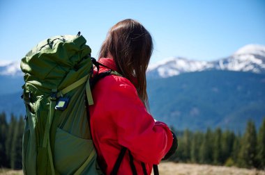 Kırmızı yağmurluk ve sırt çantalı dağ vadisinde yürüyüş yapan kadın yürüyüşçünün arka görüntüsü. Vahşi doğada macera, doğa ve seyahat yaşam tarzı.
