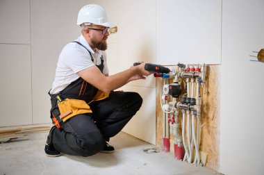 Adam yeni bir dairede ısıtma sistemini ayarlıyor. Tesisatçı merkezi sistem vanalarındaki ısıyı ayarlıyor. Servis elemanı ısıtma sistemini ayarlıyor. Yeraltı ısıtma sistemi. Adam boruyu kontrol ediyor