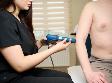 Fizyoterapist yaralı bir dirseği şok dalgası terapi cihazı ile tedavi ediyor. Yaralı tendonlar için ekstrakorporeal şok terapisi. ESWT Akustik şok dalgaları ile el fizyoterapisi.